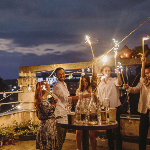 Friends celebrating with sparklers and champagne on a rooftop terrace at night