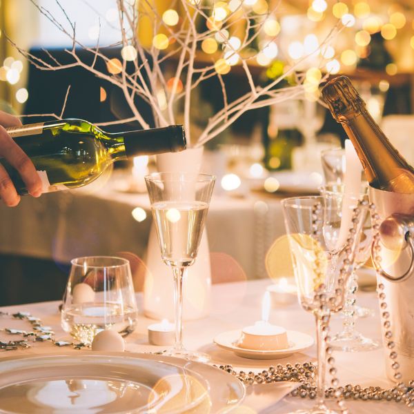 Holiday table setting with wine being poured beside a champagne bucket and string lights