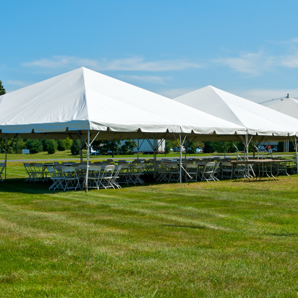 Three connected Beyond Tent frame tents over rows of tables and chairs on a grass field