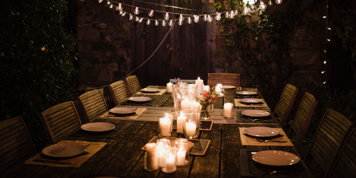 Outdoor nighttime dinner table with candle clusters and string lights against a stone wall