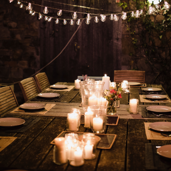Outdoor nighttime dinner table with candle clusters and string lights against a stone wall