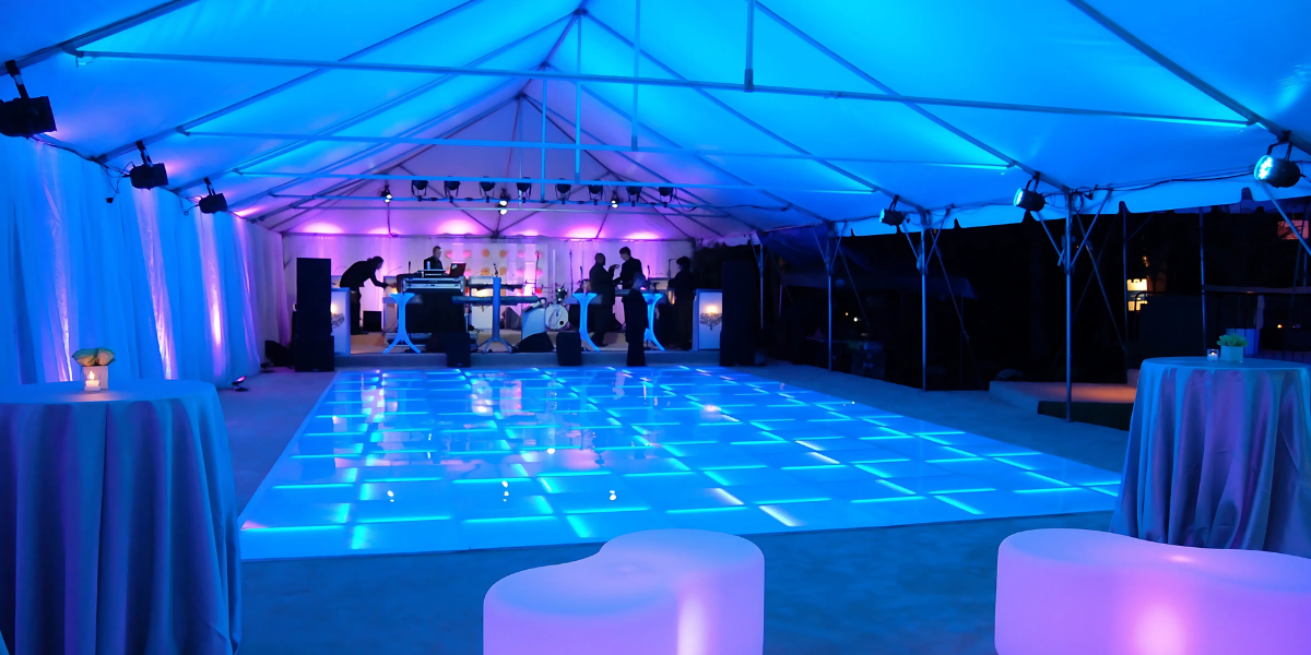 Tent interior lit blue with an illuminated LED dance floor and a DJ booth in the background