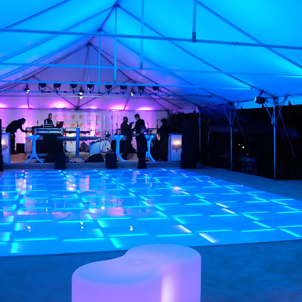 Tent interior lit blue with an illuminated LED dance floor and a DJ booth in the background