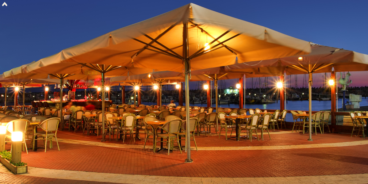 Illuminated canopy tent covering a waterfront restaurant patio with cafe tables at dusk