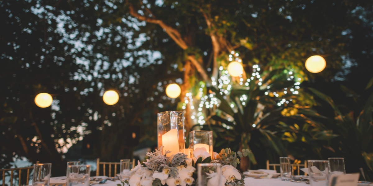 Outdoor evening reception table with candle centerpieces and glowing paper lanterns in trees