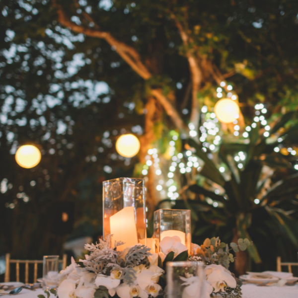 Outdoor evening reception table with candle centerpieces and glowing paper lanterns in trees