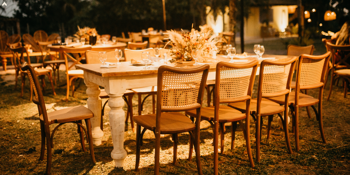 Evening reception with a whitewashed farmhouse table and rattan cane-back chairs outdoors