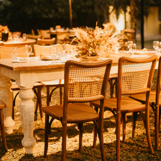 Evening reception with a whitewashed farmhouse table and rattan cane-back chairs outdoors