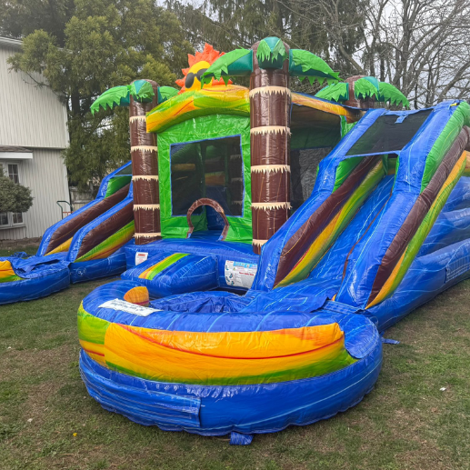 Tropical-themed inflatable bounce house and water slide combo set up on a residential lawn
