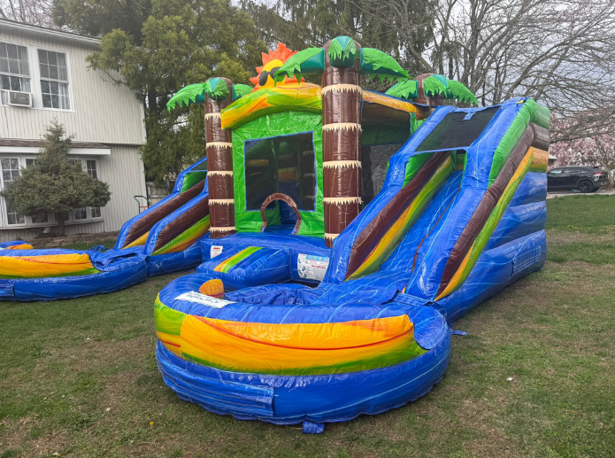 Tropical-themed inflatable bounce house and water slide combo set up on a residential lawn