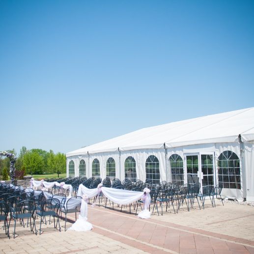 Large white frame tent with glass doors and arched windows beside rows of ceremony chairs