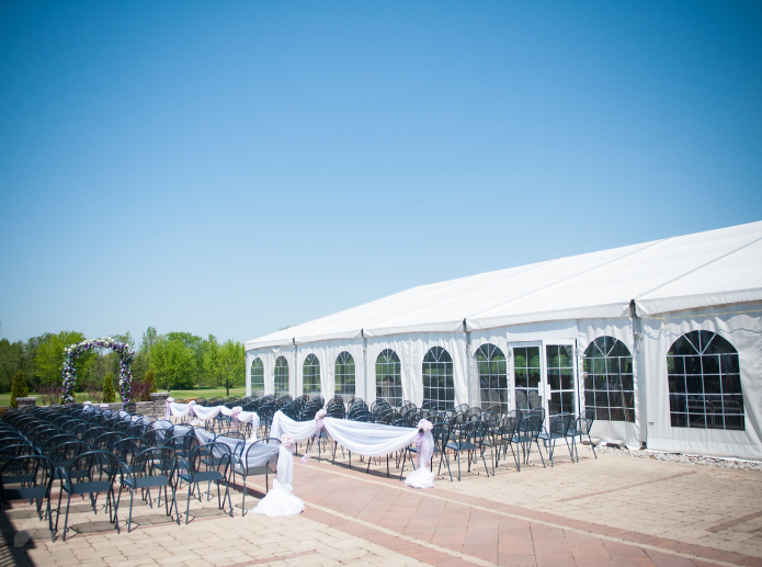 Large white frame tent with glass doors and arched windows beside rows of ceremony chairs