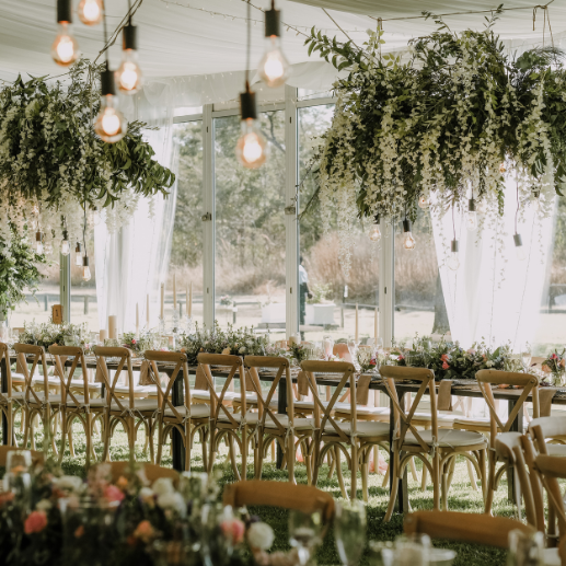 Tent interior with hanging greenery installations over a long table with cross-back chairs