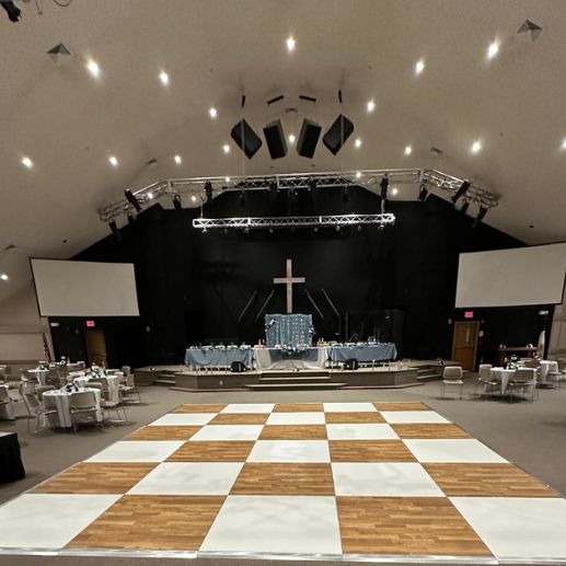 Checkered dance floor set up in a church auditorium with a stage and truss lighting
