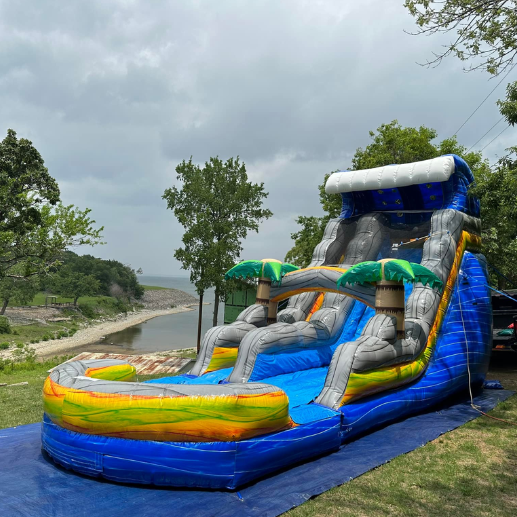 Tropical-themed inflatable water slide set up on a tarp overlooking a lake