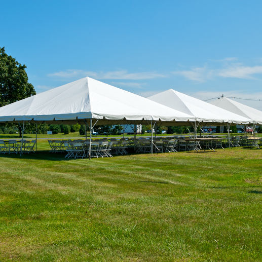 Three connected white frame tents with round tables and chairs set up on a grass field