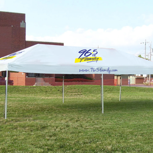 Frame tent with a custom-printed canopy advertising a local radio station on a grassy lot
