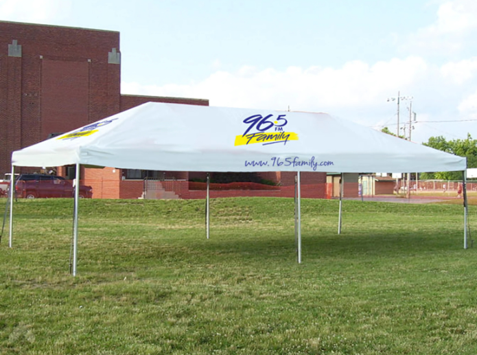 Frame tent with a custom-printed canopy advertising a local radio station on a grassy lot