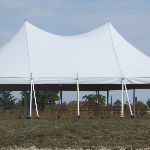 Open white pole tent with two peaks standing on a grass field under an overcast sky