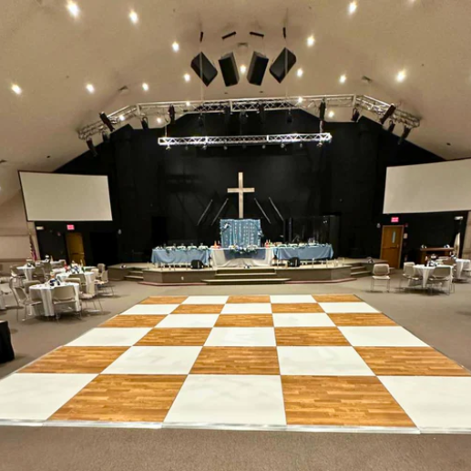 Checkered dance floor set up in a church hall in front of a stage with a cross