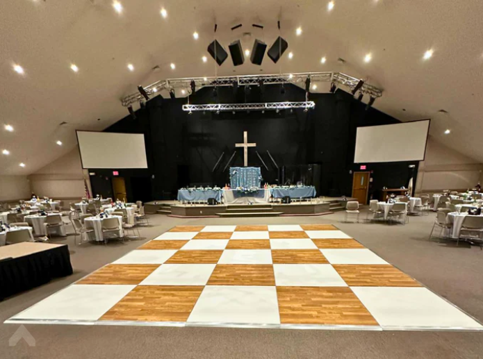 Checkered dance floor set up in a church hall in front of a stage with a cross