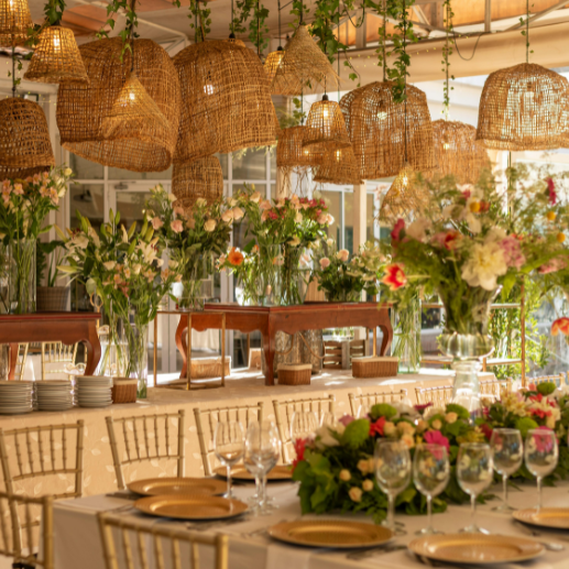 Elegant banquet table with gold chargers and chiavari chairs under hanging wicker pendant lights
