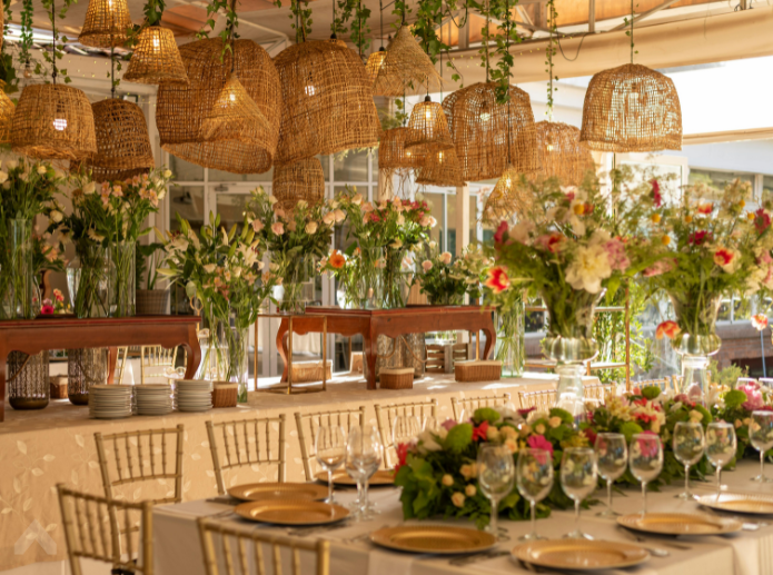 Elegant banquet table with gold chargers and chiavari chairs under hanging wicker pendant lights