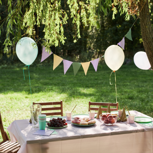 Outdoor garden party table with pastel balloons, bunting, and pastries under a willow tree