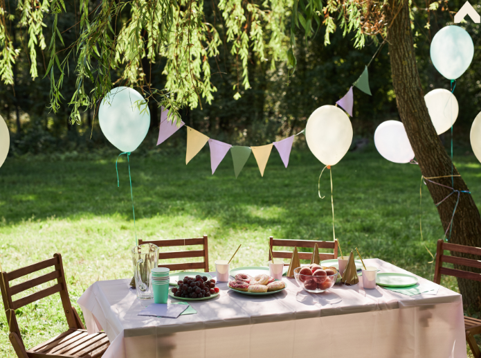 Outdoor garden party table with pastel balloons, bunting, and pastries under a willow tree
