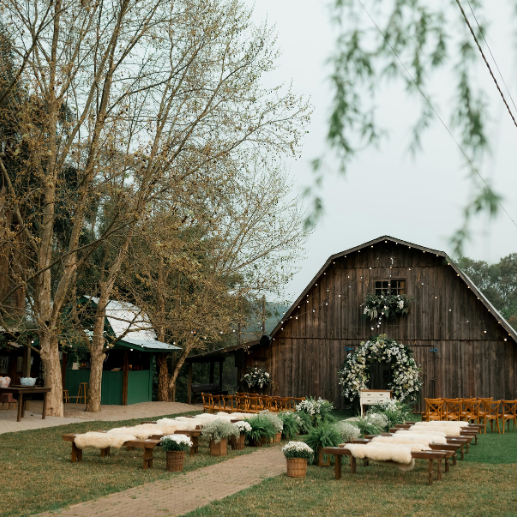 Outdoor wedding ceremony with wooden benches and sheepskin throws in front of a barn at dusk