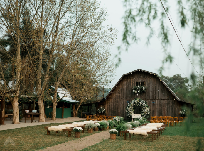 Outdoor wedding ceremony with wooden benches and sheepskin throws in front of a barn at dusk