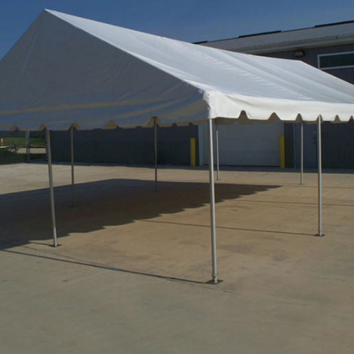 White gable-peak frame tent set up on a concrete pad beside a metal building