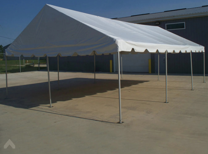White gable-peak frame tent set up on a concrete pad beside a metal building