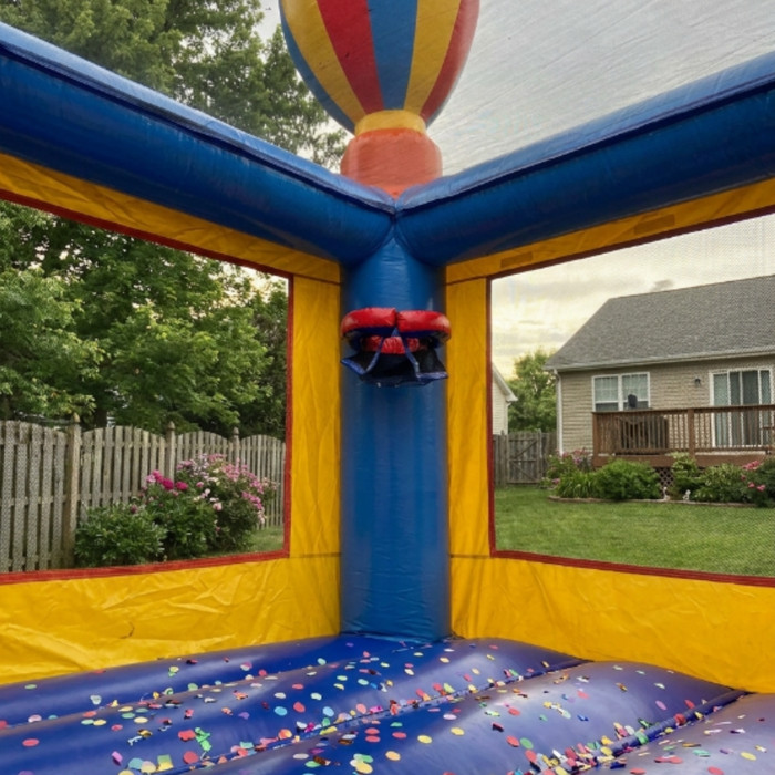 Interior perspective of the Beyond Tent 13x13 Celebration Bouncer featuring an inflatable basketball hoop and high-visibility safety mesh walls overlooking a residential backyard and wooden fence.
