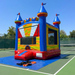 Beyond Tent 13x13 Wonder Castle commercial bounce house with blue towers and multi-color accents, secured with orange straps on a protective blue tarp over a green tennis court surface.