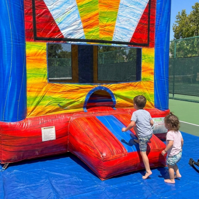 Beyond Tent 13x13 Wonder Castle commercial bounce house with blue towers and multi-color accents, secured with orange straps on a protective blue tarp over a green tennis court surface.