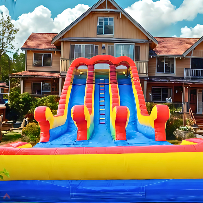 18' 2 Lane Unisex Wet & Dry Slide set up in a residential backyard, front view with ladder climb visible, large two-story house with balconies in background, blue sky with white clouds