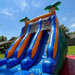 Beyond Tent 18' Double Lane Splash Wet and Dry Slide low angle view of the four wet slide lanes against a blue sky, palm tree toppers and wood privacy fence in background