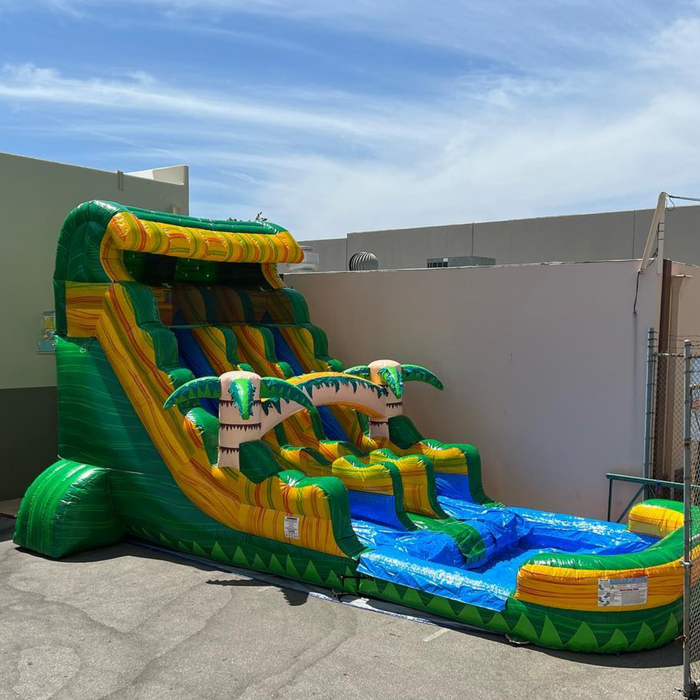 18' Dual-Lane Tropical Rush Wet/Dry Slide set up in an outdoor parking lot, tall front angle view against blue sky with wispy clouds, commercial buildings and chain-link fence