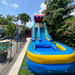 18' Rainbow slide set up on grassl in a backyard setting, featuring a blue and yellow pool base, a red and blue climbing entrance, and a blue, green, and yellow slide next to a pool. Beyond Tent photo. 
