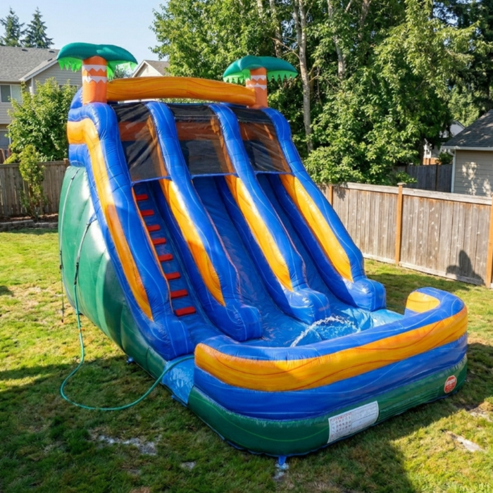 Beyond Tent 18-foot Lightweight Surf Ocean Inflatable Water Slide with dual lanes, splash pool, and blower. Shown professionally installed in a backyard setting, highlighting the vibrant blue and green PVC vinyl and palm tree accents.