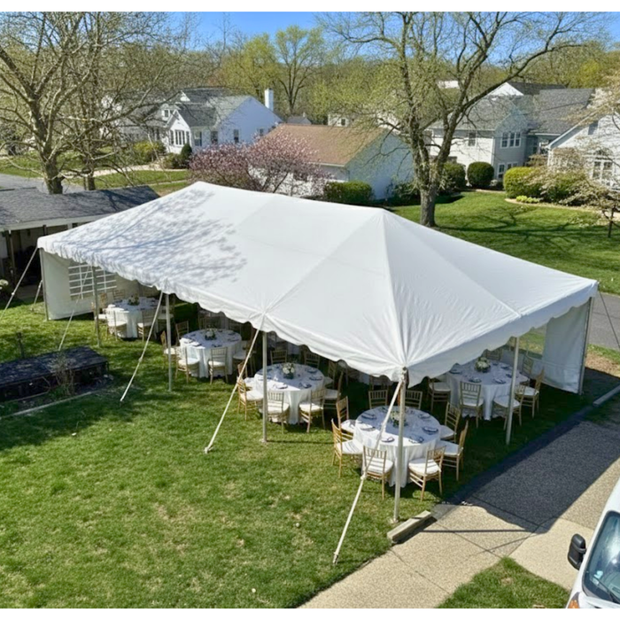Exterior view of a 20x40 white West Coast Frame Tent set up on a residential lawn, featuring white sidewalls and interior dining tables and chairs arranged for a backyard party, viewed from an elevated angle