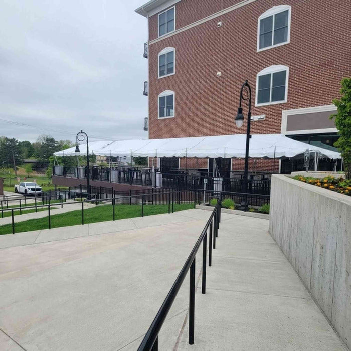 Side profile view of a large 20x50 Classic Series West Coast frame tent with a clean white canopy, installed over an outdoor commercial patio venue next to a brick building.