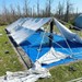Large white tent structure being set up on a blue tarp outdoors with trees in the background.
