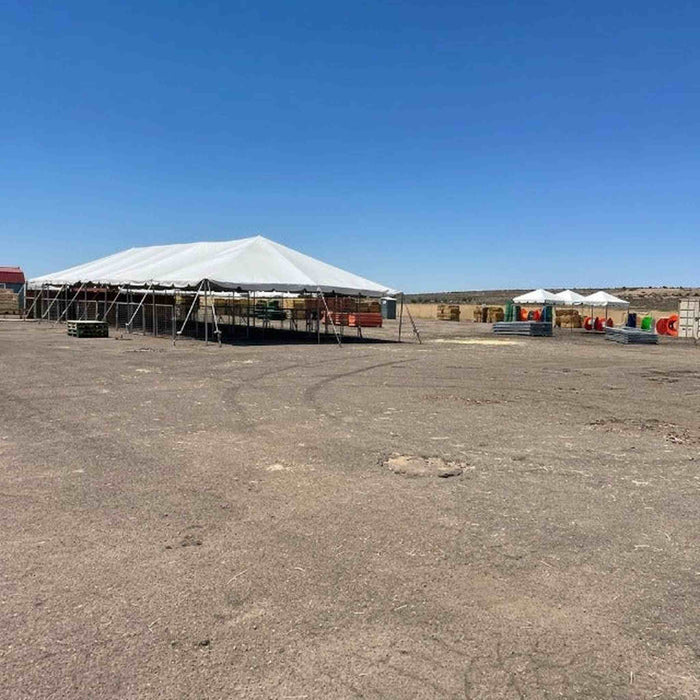 40x100 Classic Series Frame Tent frame is set up on a dusty, open desert ground under a clear blue sky. Smaller tents and equipment are visible in the background.