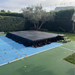 Beyond tent 4'x4' Portable Stage Platform | Heavy-Duty Commercial
set up on a tennis court with green and blue surface, surrounded by hedges and trees.