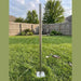 Beyond Tent Adjustable Base Plate Extension for Frame Tents standing upright on green grass in a backyard, galvanized steel pole with square mounting base plate, wood privacy fence and trees in background