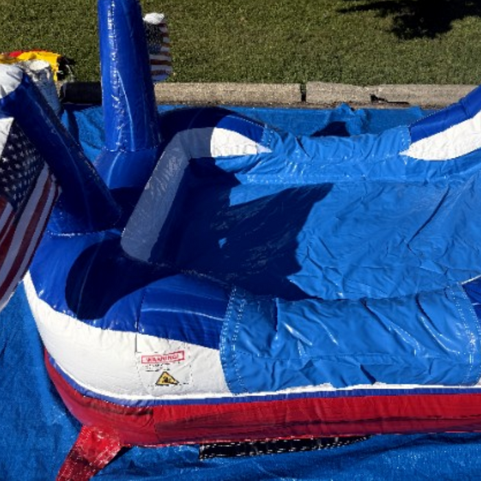 Close-up of the American Titan Wet and Dry Combo splash pool landing, blue marble vinyl with white and red trim, commercial safety label, slide end and flag holders set up on a blue tarp