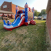 American Titan Wet and Dry Combo on a grass lawn by a brick building with patriotic bunting, single blue slide lane with white rails, splash pool with US flags, striped dome towers