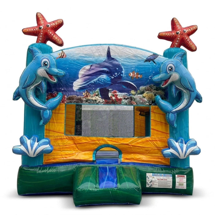 Atlantis Inflatable Castle  bounce house with an ocean theme, featuring blue dolphins, red starfish, a blue whale print on the back wall, and a green slide at the bottom, shown on a white background.